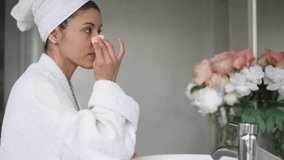 Woman in a bathrobe applies makeup to her face using a sponge while enjoying her morning routine in the bathroom - Powered by Shutterstock - Get 15% off with code: PIKWIZARD15