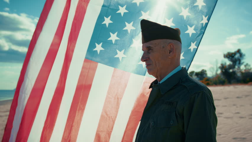 United States Veteran Looks At The Ocean From The Beach With America Flag