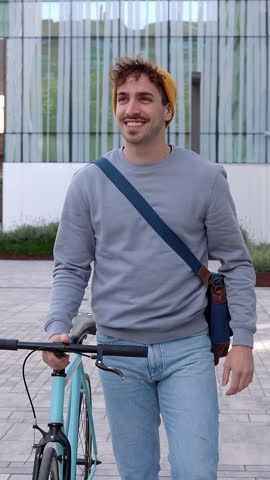 Vertical HD video of happy young student man leaving campus college after classroom riding his bicycle. Education, people and eco friendly transportation concept. 