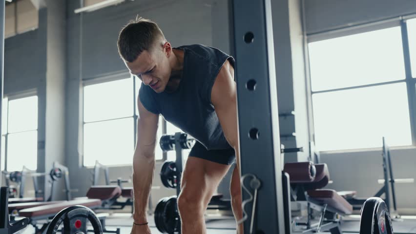 A focused man lifting weights in a contemporary gym setting, showcasing determination and physical strength during a workout session. Man Weightlifting in Modern Gym with Fitness Equipment