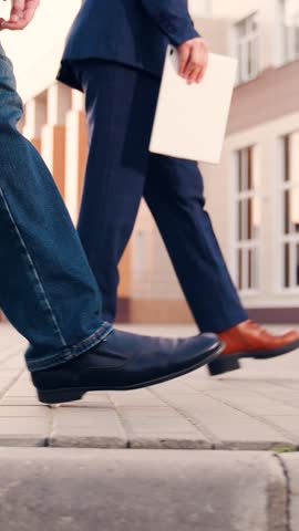 Business people walk along sidewalk, peoples walking feet. Office pedestrians walk along city street to work. City life of people. Man with briefcase in business suit walks next to business woman