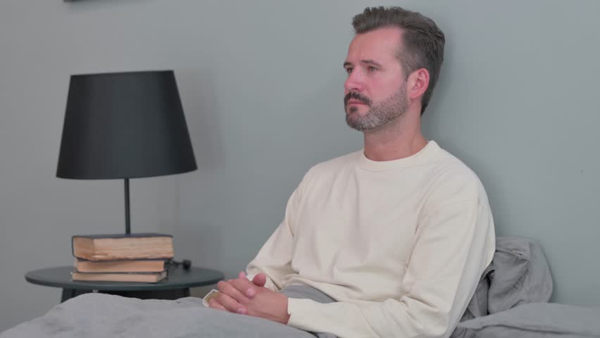 Serious Middle Aged Man Looking at Camera in Bed