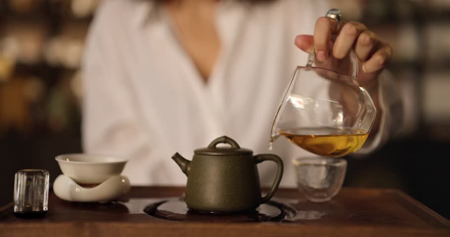 Close up a girl in a white shirt pours fresh tea over a ceramic teapot during a tea ceremony in Asian style