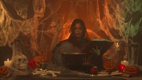 A witch in black clothing cooking a potion in a cauldron in a scary kitchen with pumpkins and a human skull and bones. - Powered by Shutterstock - Get 15% off with code: PIKWIZARD15