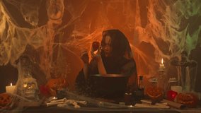 A witch in black clothing pulls a poisoned apple from a cauldron in a scary kitchen with pumpkins and human bones. - Powered by Shutterstock - Get 15% off with code: PIKWIZARD15