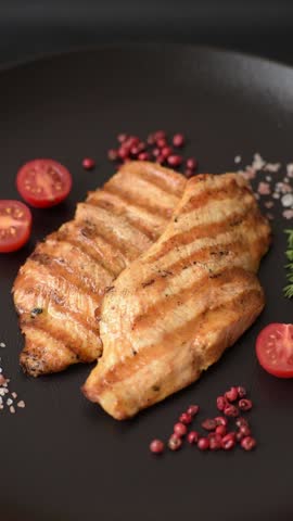 Juicy chicken fillet baked on the grill with salt, spices and herbs on a dark concrete background
