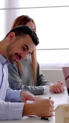 Vertical HD video. Young couple signing contract with pen after buying first property with real female agent. Two businesspeople starting professional business agreement. 