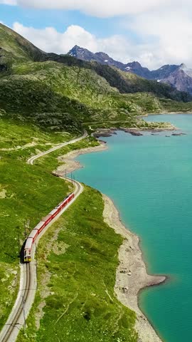 Red train on lakeside rail, Glacier Express Route, Lago Bianco in Switzerland, vertical video.