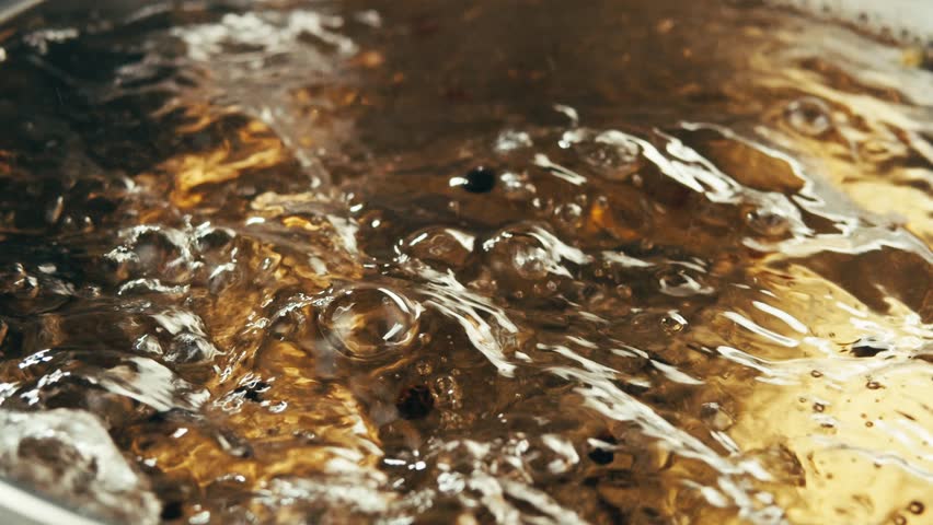 The chef in the restaurant is cooking while using the dipper in a large pot. The water is boiling and the mass of steam reflected in the morning light.