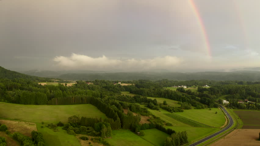 Magical rainbow over a misty countryside landscape. Enchanted forests, rolling green fields, distant hills, cloud layers, soft light, golden hour, rainy, atmospheric. Bieszczady, Poland