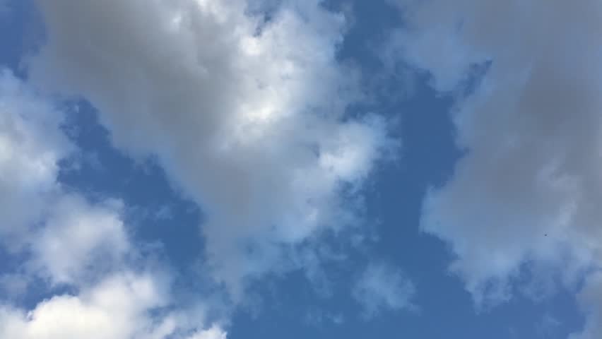 Blue sky with white and gray clouds, crows flying diagonally from the bottom right to the top left corner—first a single bird, then a group; a horizontal 4K video shot from below, can be a background.