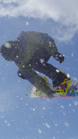 SLOW MOTION CLOSE UP: Extreme snowboarder jumping big air kicker in sunny winter in mountain snow park