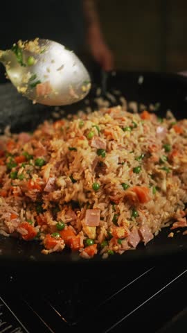 A vertical closeup footage of stirring minced beef with peas, rice and chopped carrots in a frying wok, with blurred background