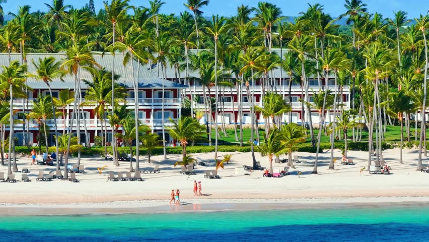Blue ocean by white sand beach. Tropical resort nature with palm trees. Caribbean sea and sky. Small wild sun loungers. Beach hotel landscape. Turquoise water of Atlantic ocean.