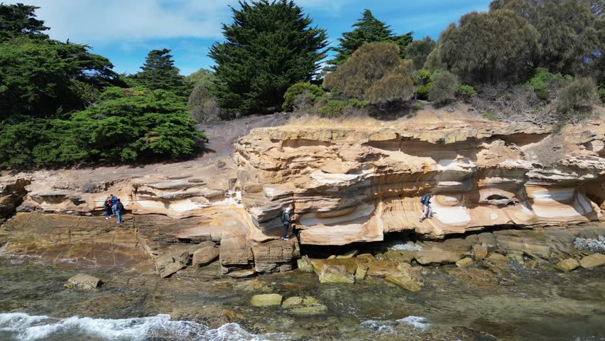 An aerial footage of small group of people visiting the Painted Cliffs on Maria Island, on a sunny day in Tasmania, Australia