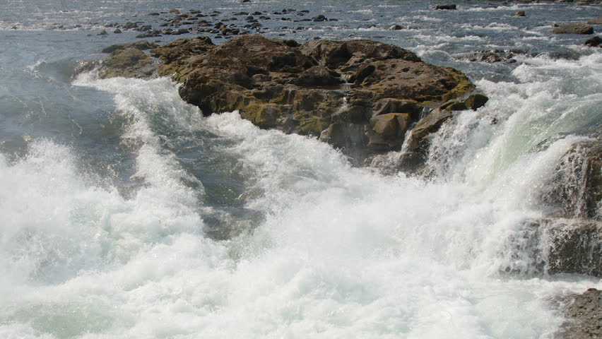 Slow motion whitewater pouring over high flow waterfall, rock island