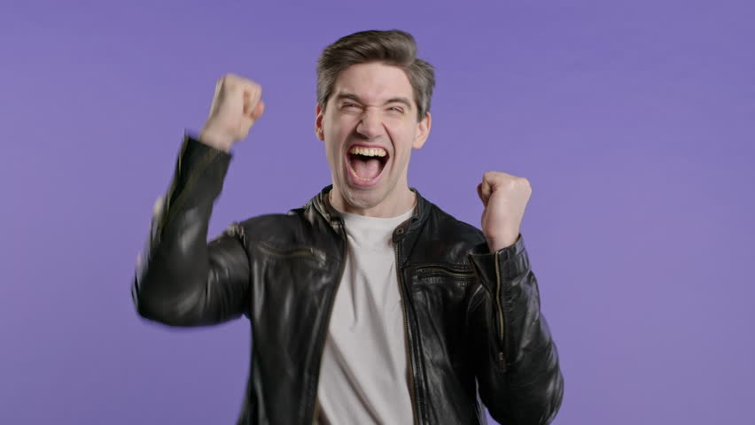 Handsome man on violet,shows triumph yes YEAH gesture of victory,achieved result
