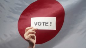 Woman holding title sign with text Vote on japanese flag background. General elections in Japan, prime ministers, citizen duty - Powered by Shutterstock - Get 15% off with code: PIKWIZARD15