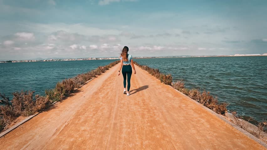 A woman walks between two lakes on a narrow dirt road