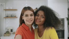 Happy interracial lesbian couple smiling hugging and using a smartphone video call having fun and cheerful in kitchen room at home. Black female and girlfriend LGBTQ pride taking selfies together.  - Powered by Shutterstock - Get 15% off with code: PIKWIZARD15