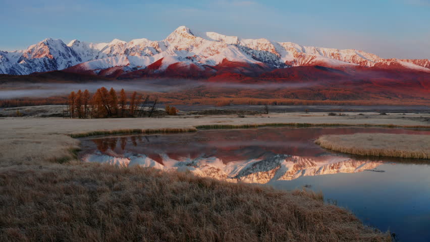 Pan left of snow-capped mountain peaks reflected in the lake at dawn at late autumn in Mountain Altai, showcasing vibrant landscapes