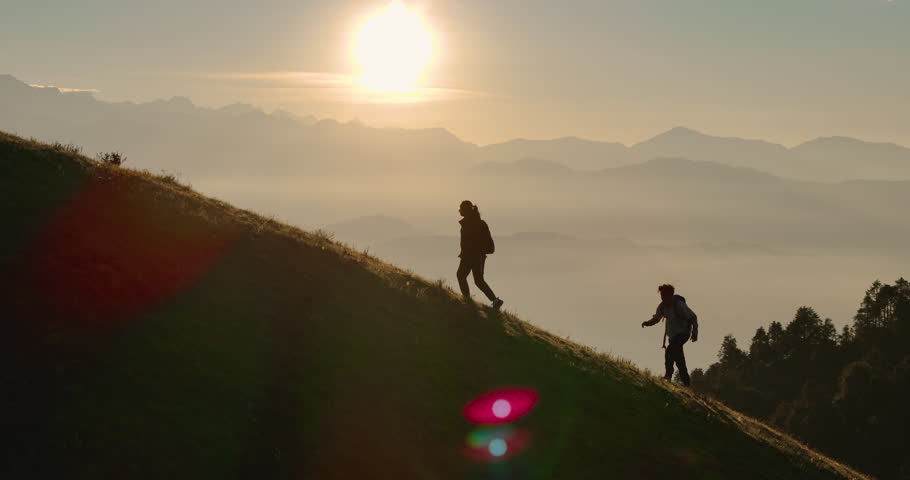 Drone shot captures couple hiking along trekking trails of Nepal enjoy quality time together as sunrays lens flare and horizon with mountain ranges enhance beauty of the Shailung Dolakha scene