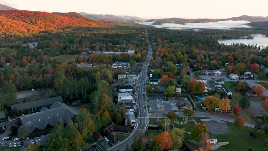 Time-lapse of Schroon Lake, NY, capturing the changing light over autumn-colored trees, the small town, and surrounding hills, with fog drifting over the landscape.