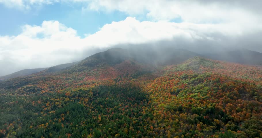 Sunlight breaks through drifting clouds over a vibrant autumn mountain, showcasing the beauty of God