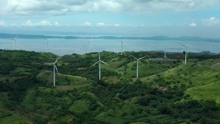 Aerial lateral wide shot of wind farm with wind turbines on coast of Philippines in Pililla Rizal. Cloudy stormy day with sea in background.