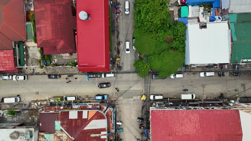 City intersection with cars driving on the streets, surrounded by buildings with red roofs and a large tree in the center in Manila, Philippines