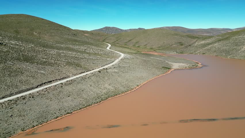 Aerial view: Moto rides dirt road past muddy lagoon in Peru foothills