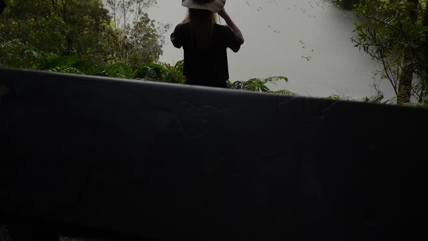 Explorer in hat uses binnoculars overlooking Lake Matheson in lush New Zealand rainforest, peaceful and scenic environment