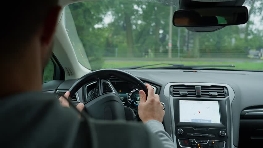 Man driving car on rainy day, maintaining focus on road. Male driver driving car looking around at road traffic and turning steering wheel. Safety ride
