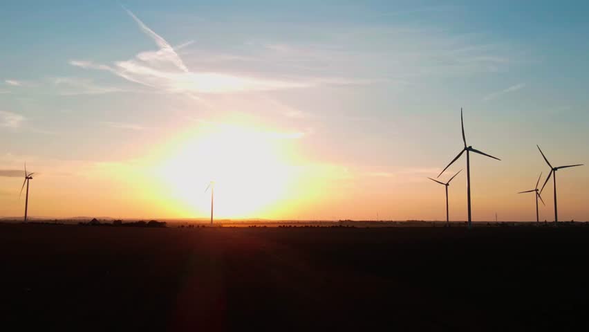 Silhouetted wind turbines in countryside landscape during sunset. Wind power plant generating clean energy. Concept of renewable and sustainable energy