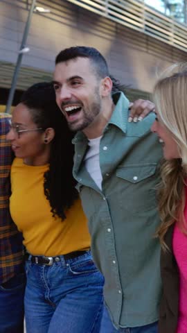 Vertical HD video of happy group of multiracial friends laughing while walking together at city street. Millennial student people enjoying free time having fun outdoors. Youth community concept.
