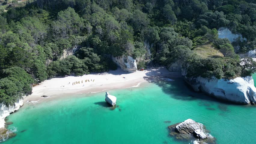 An aerial footage of a group of tourists visiting the scenic Cathedral Cove Beach on a sunny day in Hahei, New Zealand