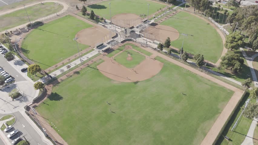 An aerial footage of players in baseball pitch during the daytime with a nearby road, at the fairgrounds of Costa Mesa, California
