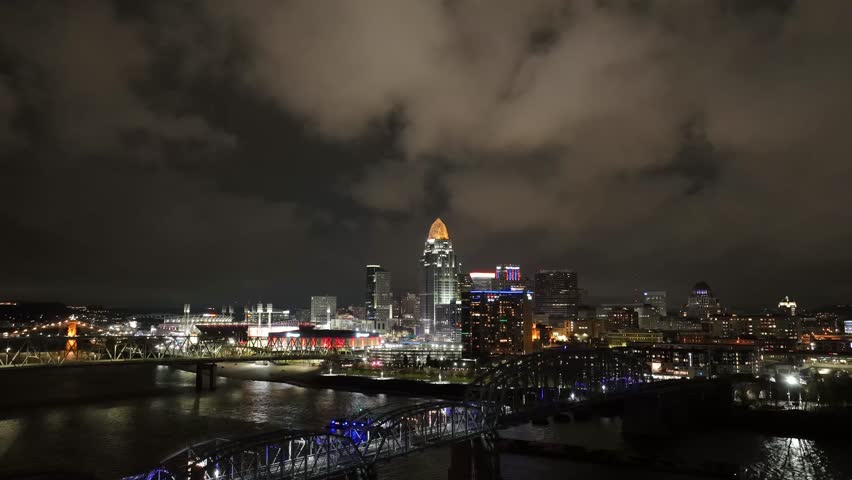 A drone timelapse of illuminated Cincinnati Metropolitan area at night along the Ohio River with cloudy sky in the US