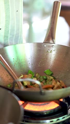 A closeup vertical slow-motion of a chef adding and ingredient to vegetables in cooking pot on the stove, during cooking class in Thailand