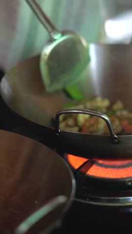 A closeup slow-motion vertical of a hand cooking pad Thai in cooking pot on the stove, during cooking class in Thailand