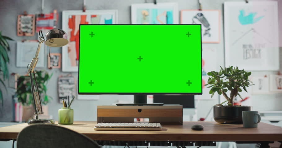 Desktop Computer Monitor on a Wooden Desk with a Green Screen Chroma key Mock Up Display. Office Working Station for Art, Enginering, Fashion, Architectural, Creative Agency. Template For Advertising.