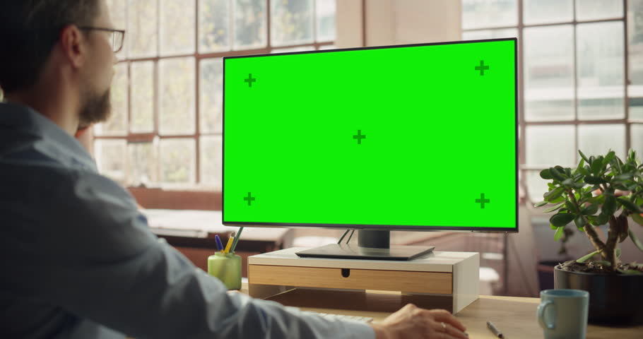 Professional Black Female Using Green Screen Monitor for Content Creation. Creative working on Chroma Key Display. Modern Home Office with Minimalist Interior. Over the Shoulder Shot Static Shot