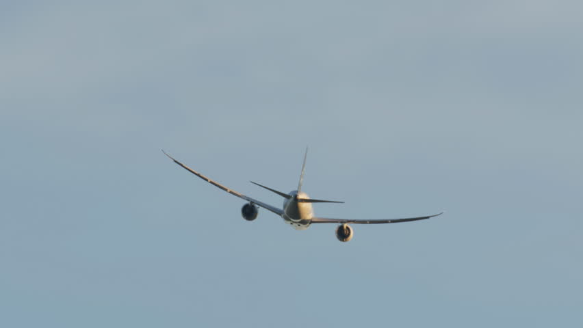 A rear view of a commercial airplane flying at high altitude with a clear blue sky in the background. The aircraft's engines and wings are visible as it moves away from the camera