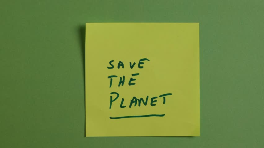 A person is placing a sticky note on a green background. Written on the sticky note are the words Save The Planet. Concept, sustainability, ecology, climate. Slow motion.