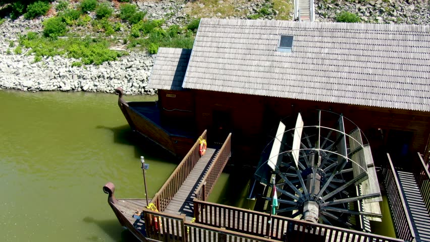 Tracking aerial past large water wheel on ship mill, a floating lumber mill powered by Danube River.