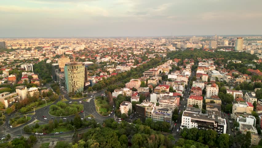 High angle drone footage of Herastrau and Arcul de Triumf in Bucharest Romania. Green park shot on a sunny day during golden hour. Cityscape of warm summer evening. Rugby stadium visible from above