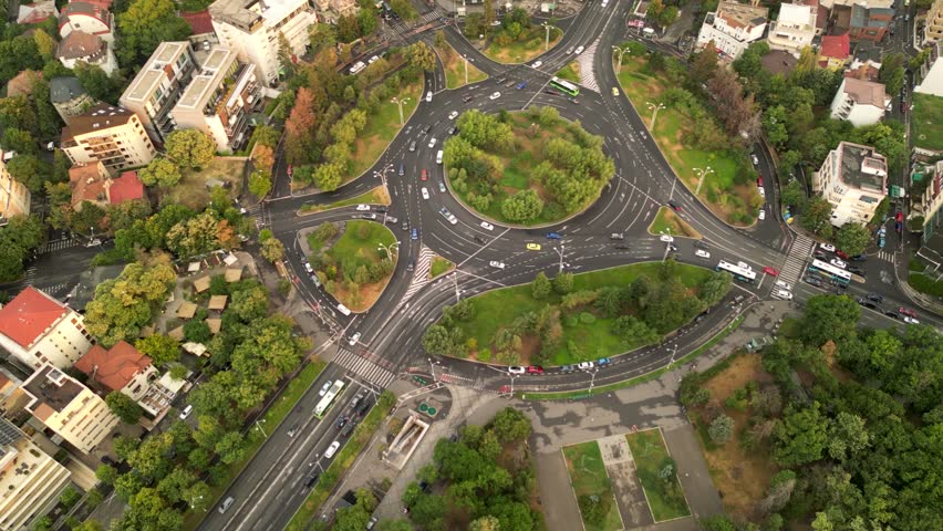 High angle drone footage of Herastrau and Piata aviatorilor Bucharest Romania. Green roundabout seen on a sunny day during golden hour. Traffic navigating a rotary intersection. Flowing traffic.