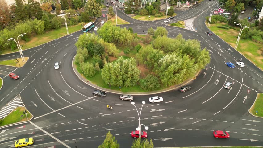 High angle drone footage of Herastrau and Piata aviatorilor Bucharest Romania. Green roundabout seen on a sunny day during golden hour. Traffic navigating a rotary intersection. Flowing traffic.