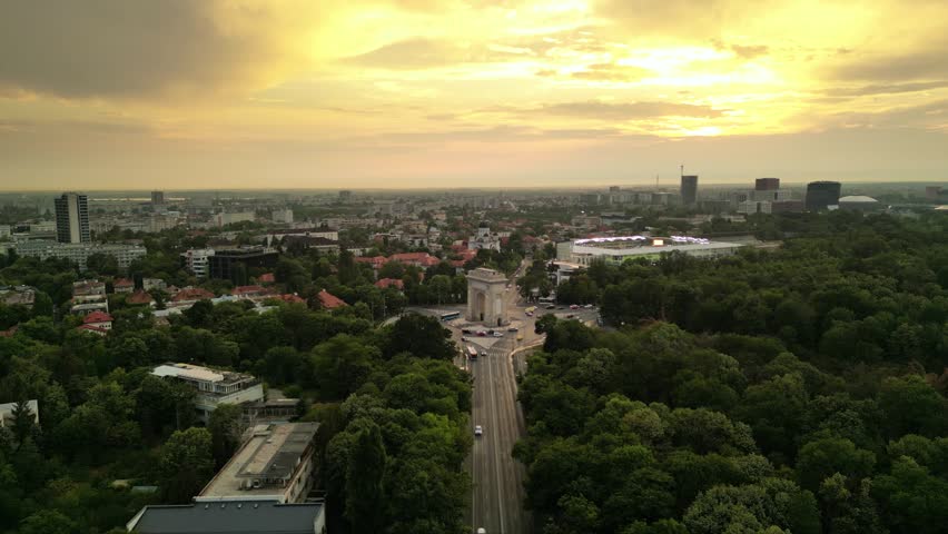 High angle drone footage of Herastrau and Arcul de Triumf in Bucharest Romania. Green park shot on a sunny day during golden hour. Cityscape of warm summer evening. Rugby stadium visible from above