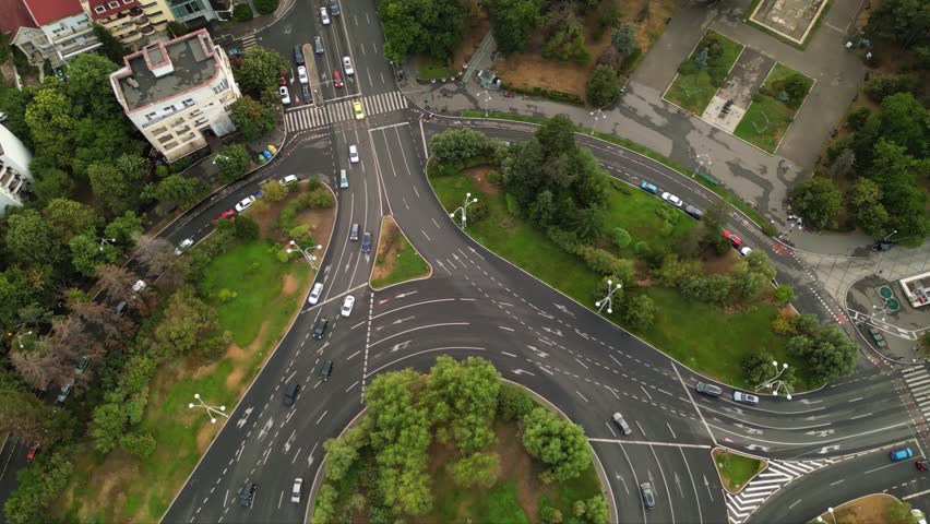 High angle drone footage of Herastrau and Piata aviatorilor Bucharest Romania. Green roundabout seen on a sunny day during golden hour. Traffic navigating a rotary intersection. Flowing traffic.